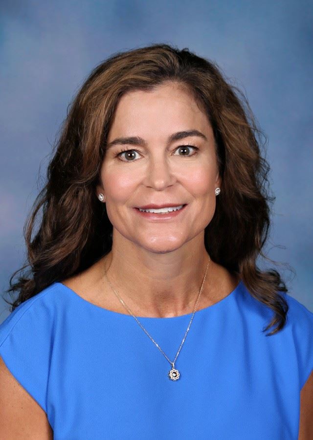 Principal, Dr. Anna Crawford, with her brown hair worn down wearing a blue dress.